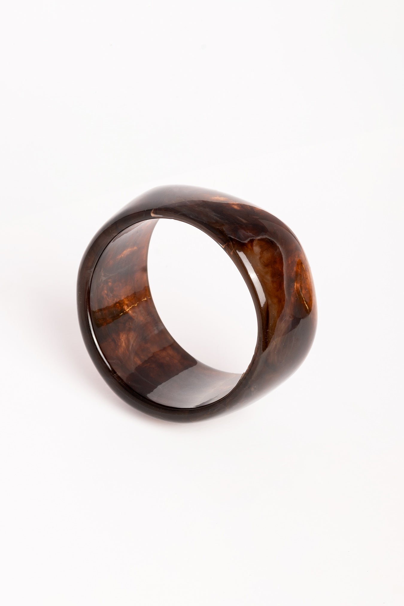 “Brazalete Lola de resina en tonos marrón oscuro, en posición inclinada sobre fondo blanco para resaltar su forma redondeada.”