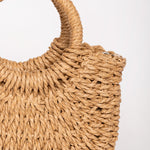 Detalle de la textura trenzada y el asa redonda del bolso de rafia camel.
