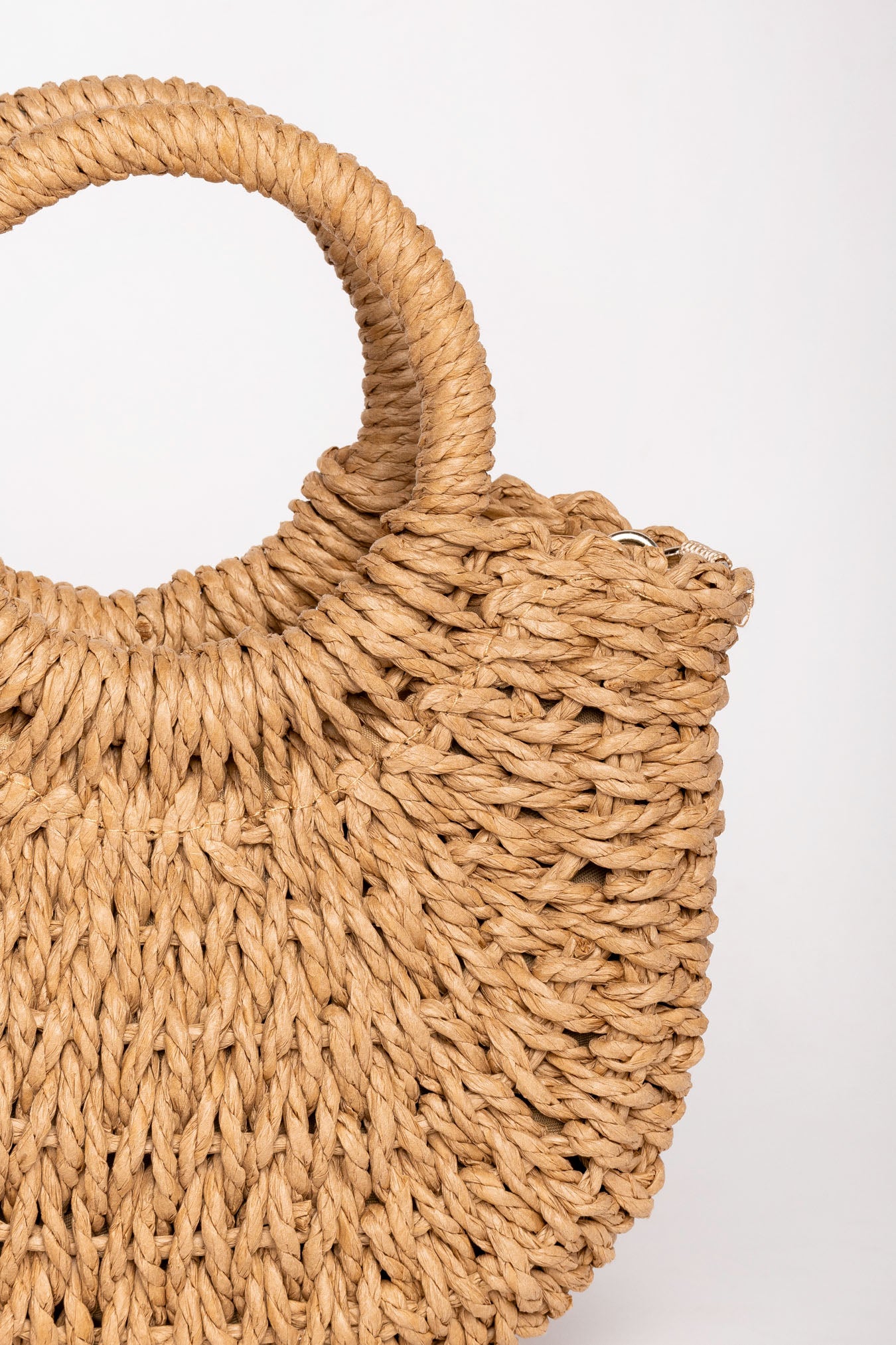 Detalle de la textura trenzada y el asa redonda del bolso de rafia camel.