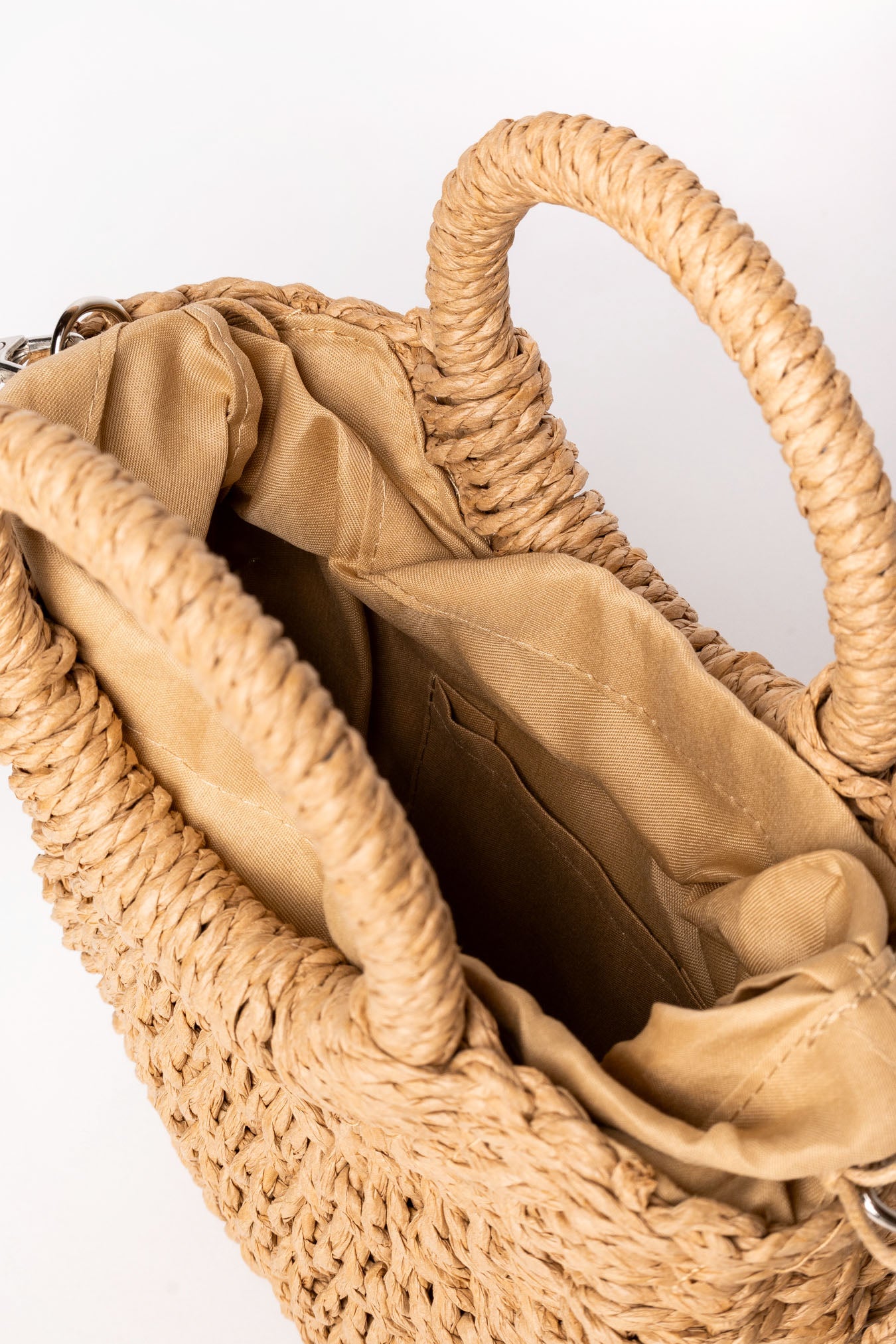 Detalle del interior del bolso de rafia camel mostrando bolsillo interior y forro de tela.