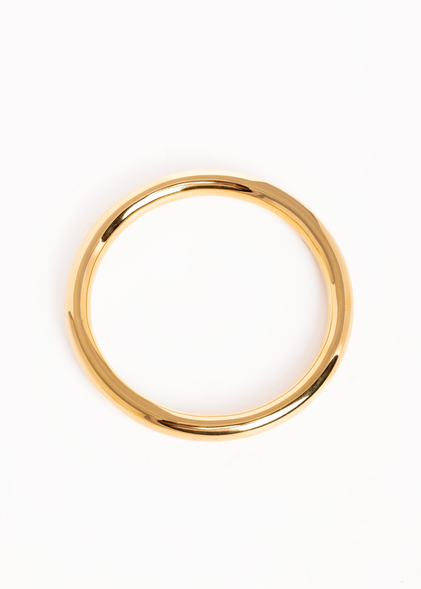 “Brazalete dorado brillante en posición inclinada sobre superficie blanca, mostrando su forma redondeada.”