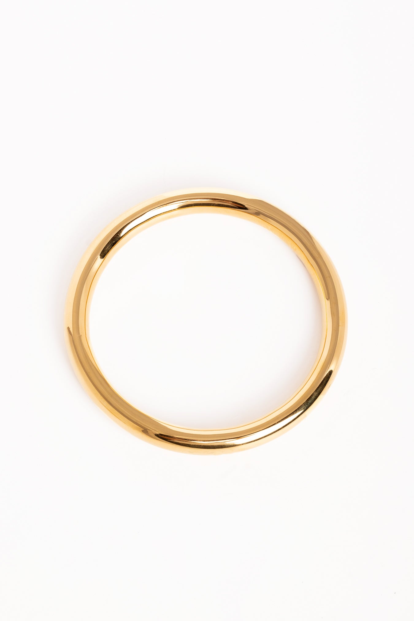 “Brazalete dorado brillante en posición inclinada sobre superficie blanca, mostrando su forma redondeada.”