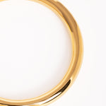 Plano detalle del brazalete dorado, destacando su superficie pulida y curvatura elegante.”