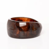 “Plano detalle del Brazalete Lola de resina marrón oscuro, destacando su superficie pulida y textura marmoleada.”