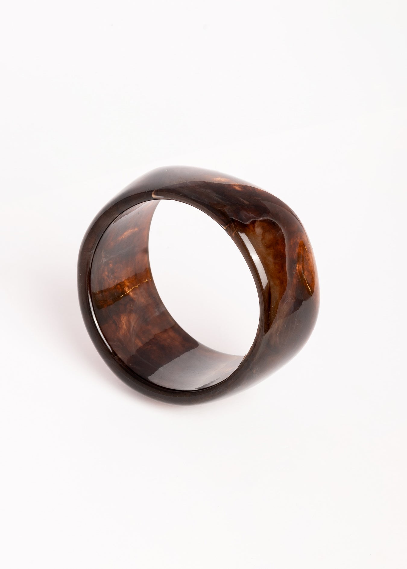 “Brazalete Lola de resina en tonos marrón oscuro, en posición inclinada sobre fondo blanco para resaltar su forma redondeada.”