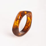 “Brazalete Regina Ámbar de resina con efecto marmoleado, en vista superior sobre fondo blanco.”