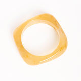 “Brazalete Regina Beige en posición vertical, mostrando su forma cuadrada y textura translúcida sobre fondo blanco.”