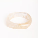 “Brazalete de resina efecto mármol en tono marfil, con forma cuadrada y bordes redondeados, fotografiado sobre fondo blanco.”