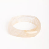 “Brazalete de resina efecto mármol en tono marfil, con forma cuadrada y bordes redondeados, fotografiado sobre fondo blanco.”