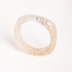  “Brazalete marfil de resina con textura marmoleada, capturado en vista superior sobre superficie blanca.”