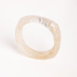  “Brazalete marfil de resina con textura marmoleada, capturado en vista superior sobre superficie blanca.”