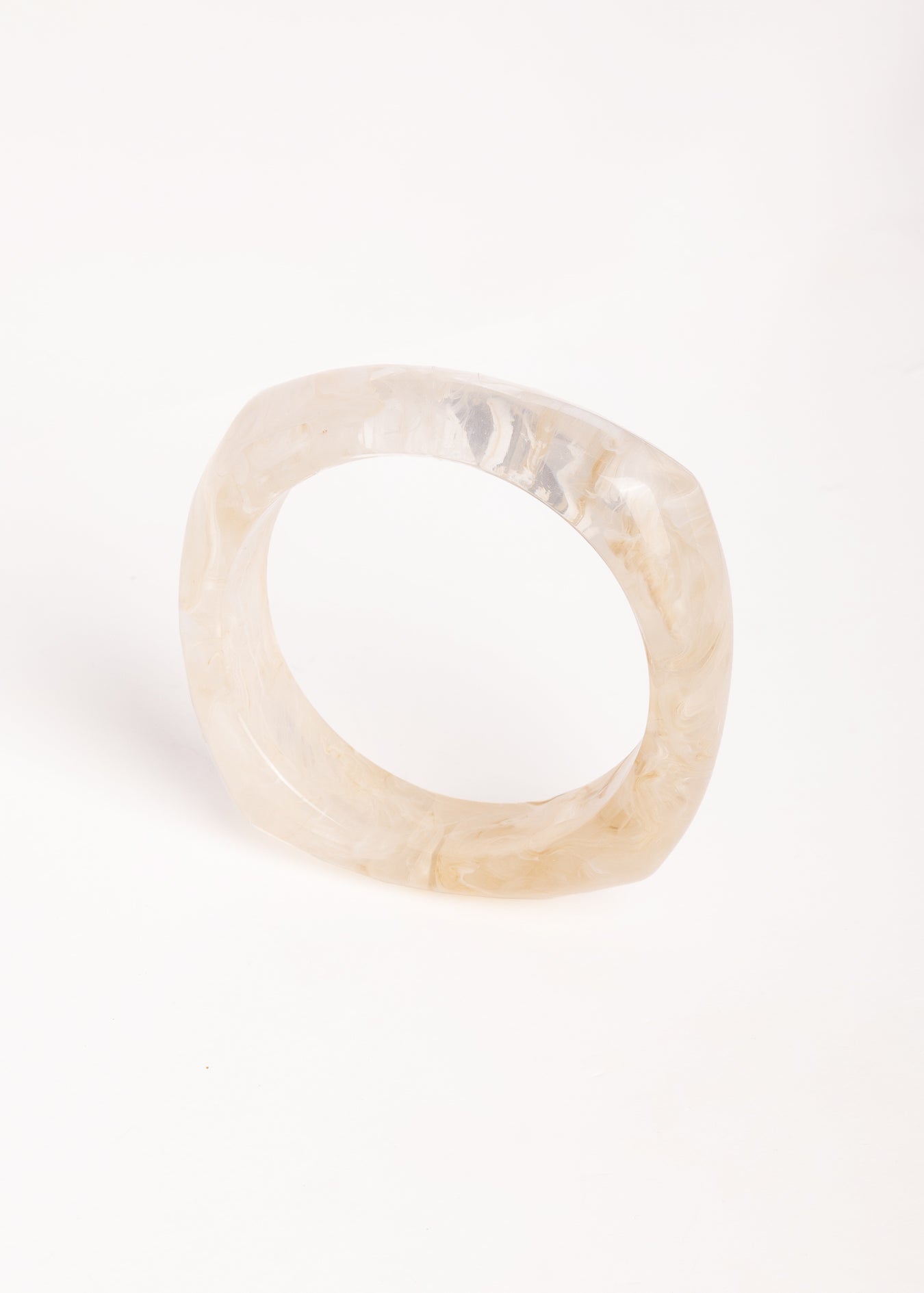  “Brazalete marfil de resina con textura marmoleada, capturado en vista superior sobre superficie blanca.”