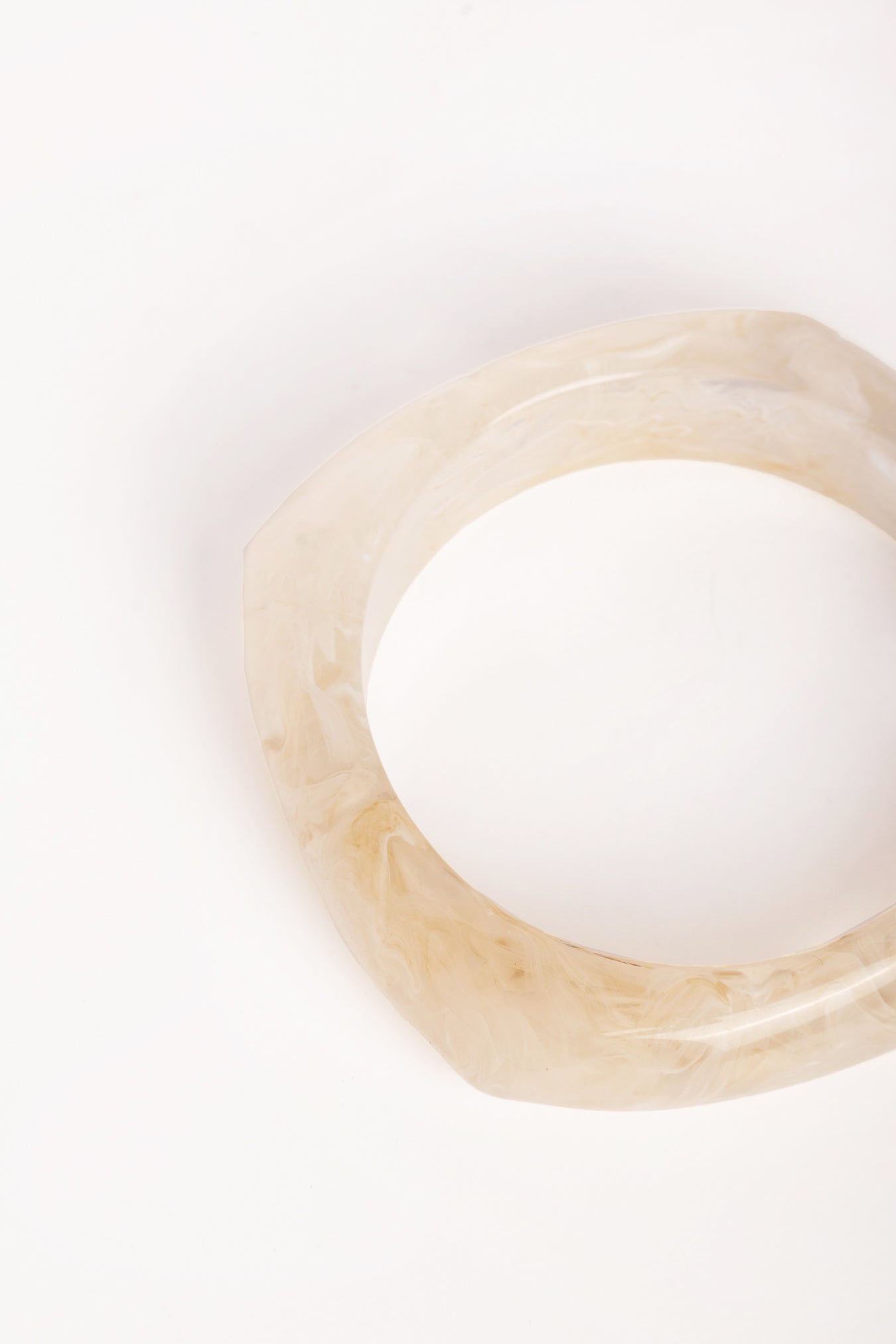  “Plano detalle del brazalete de resina marfil, mostrando su acabado traslúcido y forma geométrica.”