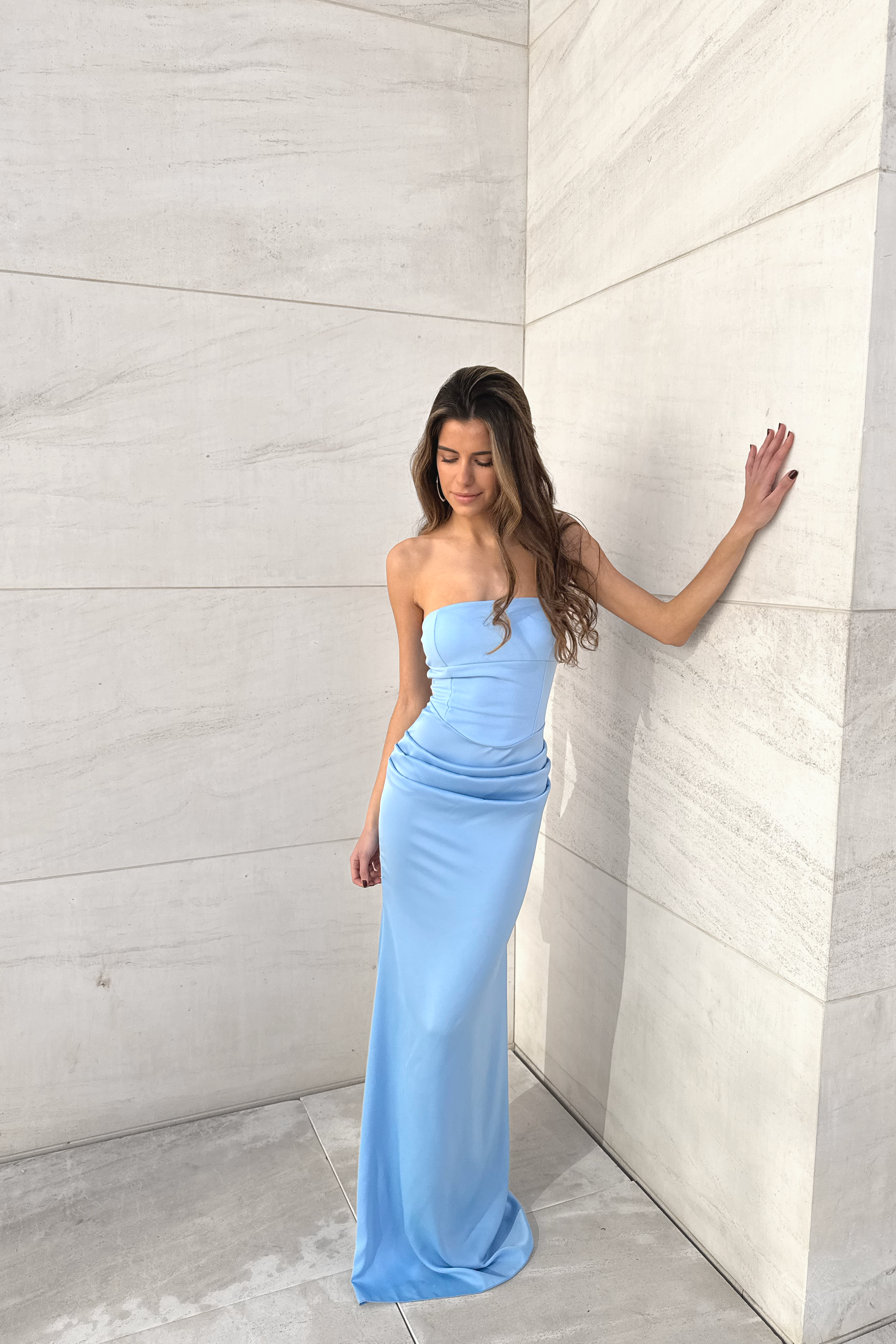 Modelo con vestido largo celeste palabra de honor, de silueta entallada con drapeado en la cadera.