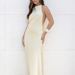 Vista frontal de modelo con vestido largo amarillo de satén escote halter.