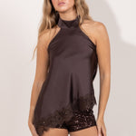 Modelo vistiendo un top satinado marrón con cuello halter y encaje en el bajo, combinado con mini short de lentejuelas marrón