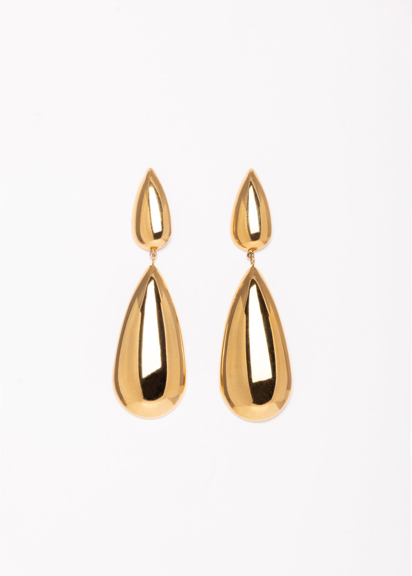 “Pendientes Kalma Oro dispuestos de manera simétrica sobre fondo blanco, mostrando su acabado brillante y diseño elegante.”