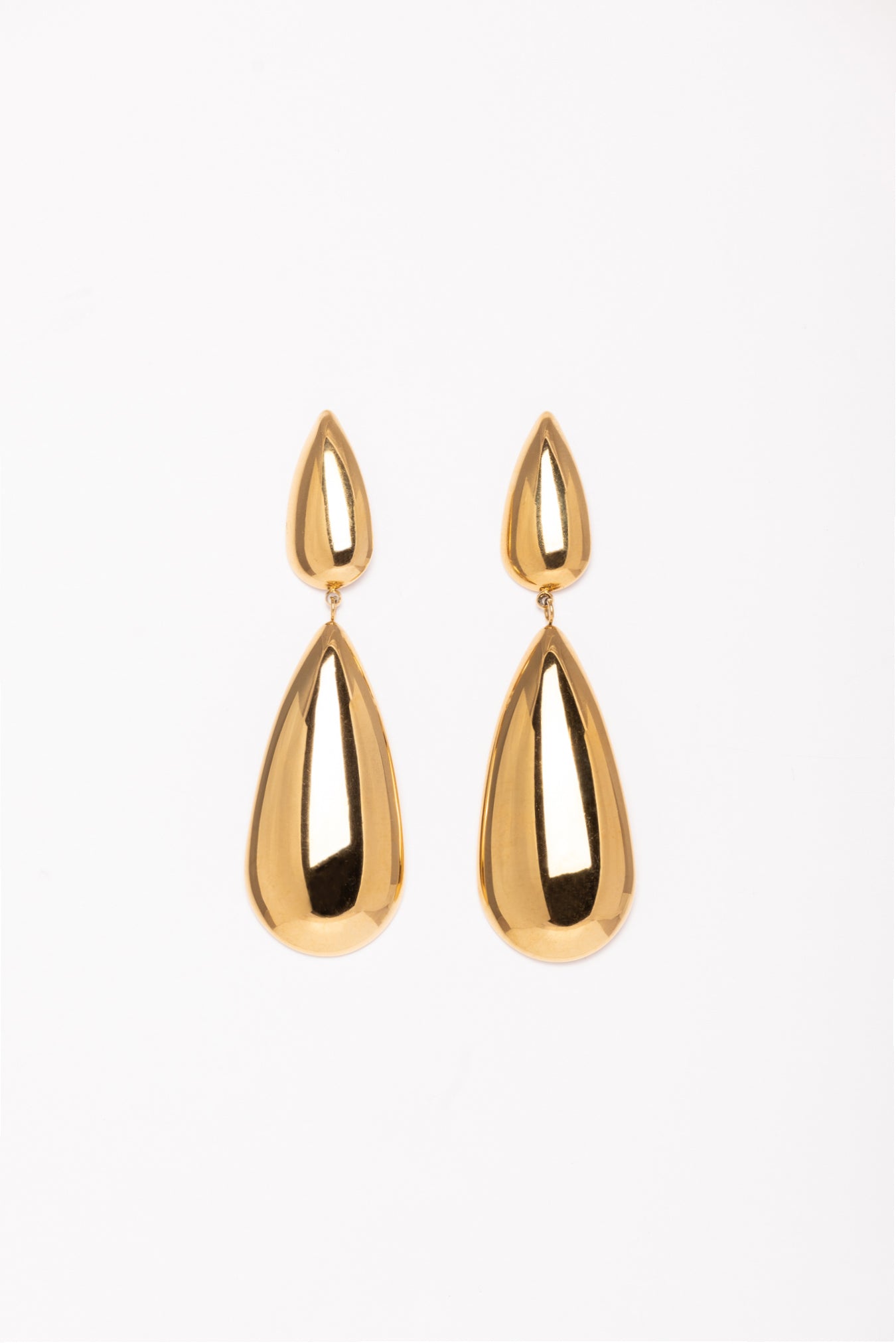 “Pendientes Kalma Oro dispuestos de manera simétrica sobre fondo blanco, mostrando su acabado brillante y diseño elegante.”