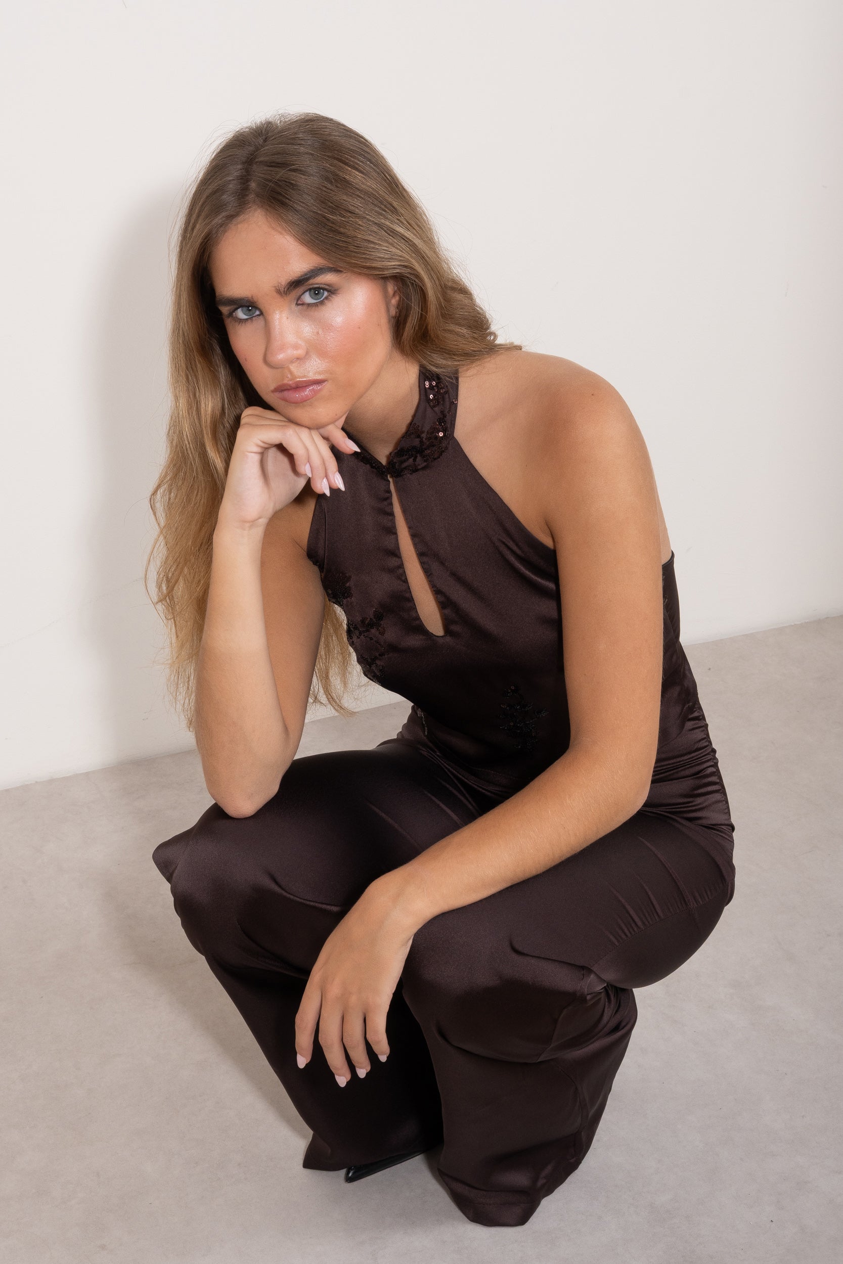 Top halter marrón satinado con detalle de abertura y lentejuelas, modelo agachada posando con pantalón a juego