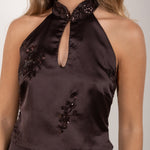 Detalle  del escote  del top halter marrón satinado con detalle de abertura y lentejuelas, modelo de pie posando.