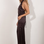 Top halter marrón satinado con detalle de abertura y lentejuelas, modelo de pie posando con pantalón a juego