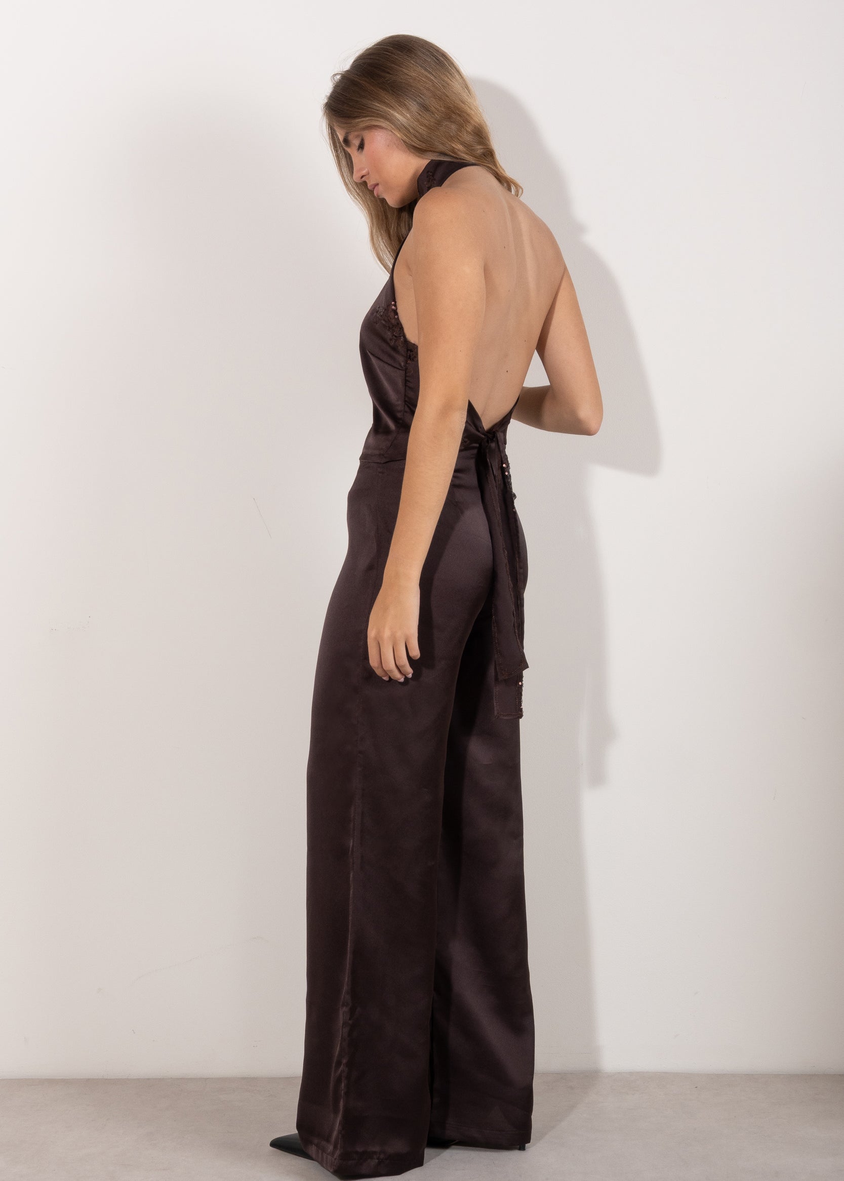 Top halter marrón satinado con detalle de abertura y lentejuelas, modelo de pie posando con pantalón a juego