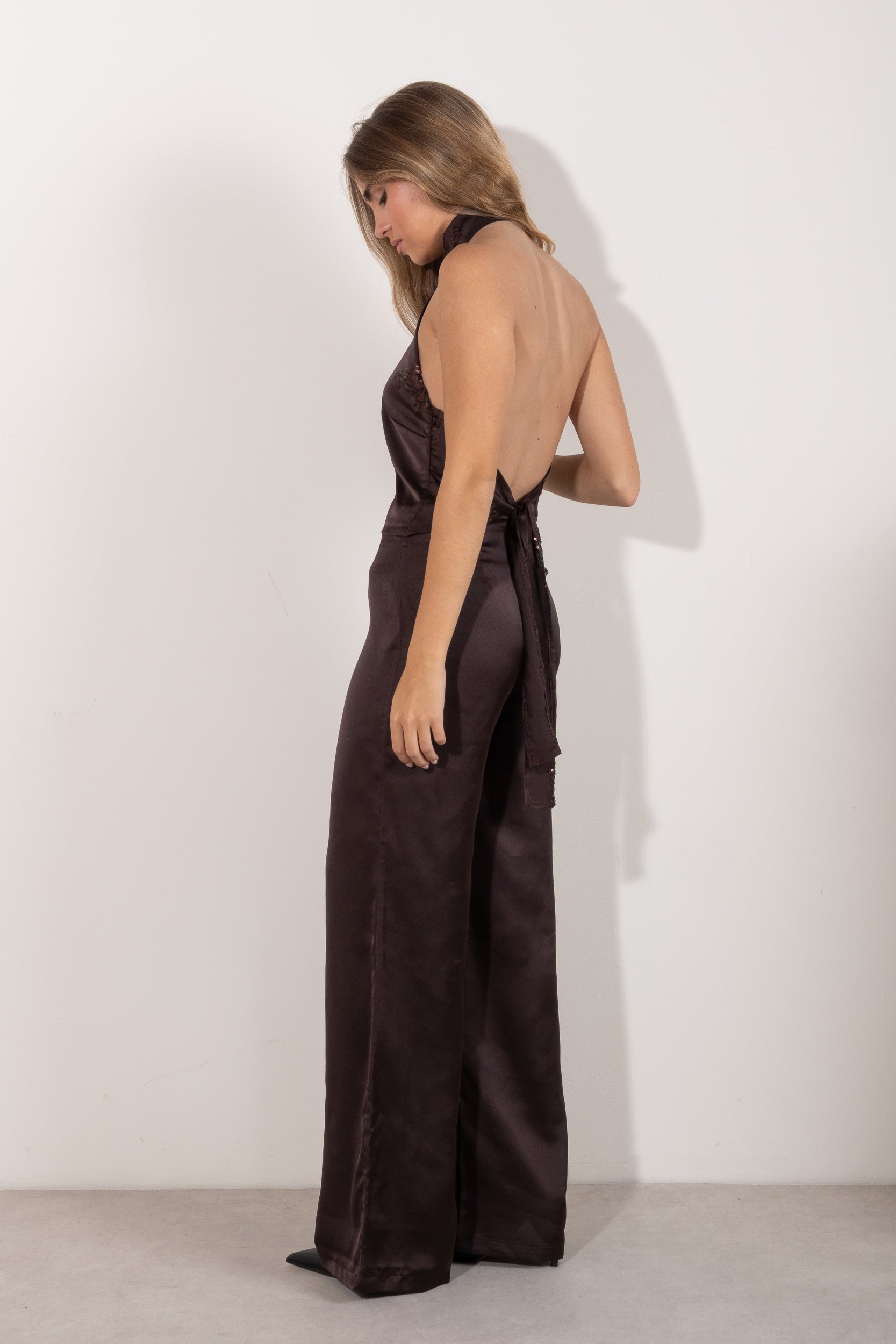 Top halter marrón satinado con detalle de abertura y lentejuelas, modelo de pie posando con pantalón a juego