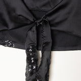 Detalle parte trasera del top negro halter con abertura central y lazo ajustable, decorado con detalles de lentejuelas