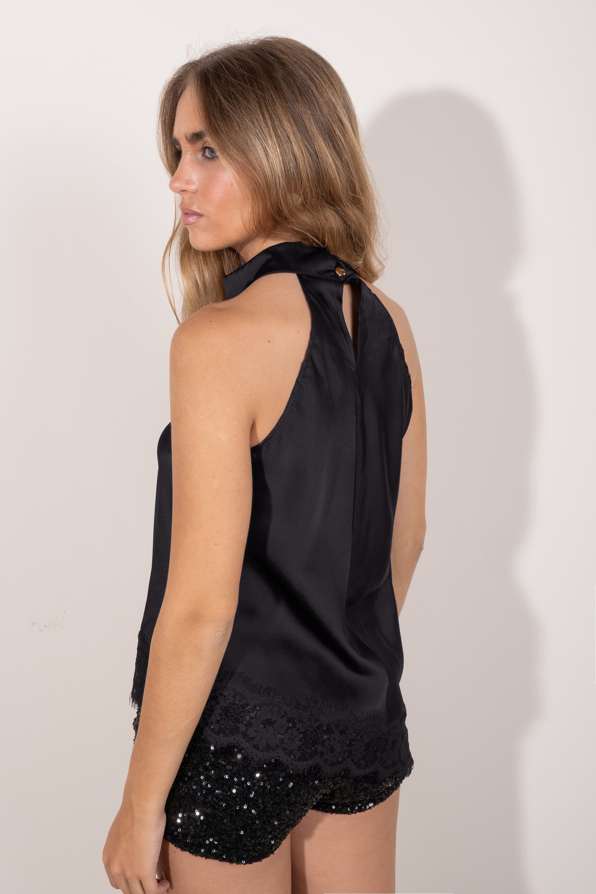 Espalda de  top negro satinado con cuello halter y detalle de encaje en el bajo.