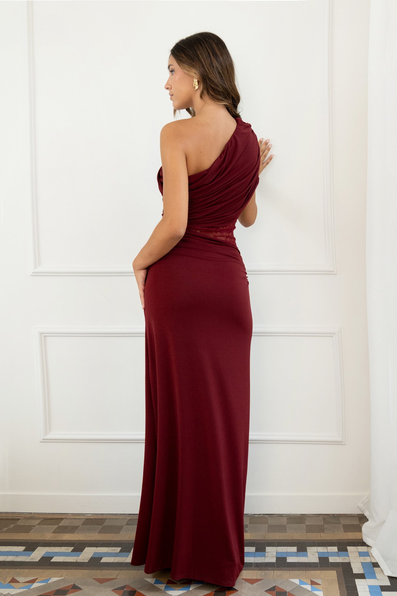 modelo con vestido largo granate de fiesta perfecto para eventos especiales, bodas, galas o cenas formales. Diseño asimétrico de un solo hombro. La silueta entallada resalta la figura, mientras que la sutil franja de encaje floral en la cintura añade un toque romántico y sensual, sin perder la clase.
Detalle: Encaje semitransparente en la cintura