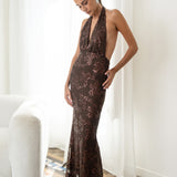 Modelo con vestido Fiori Marrón su escote halter atado al cuello y su espalda descubierta aportan un aire sofisticado y moderno. Confeccionado en gasa ligera decorada con lentejuelas.