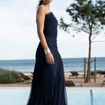 Vista lateral de Martina caminando con el vestido azul noche, mostrando la caída de la falda y los tacones plateados.