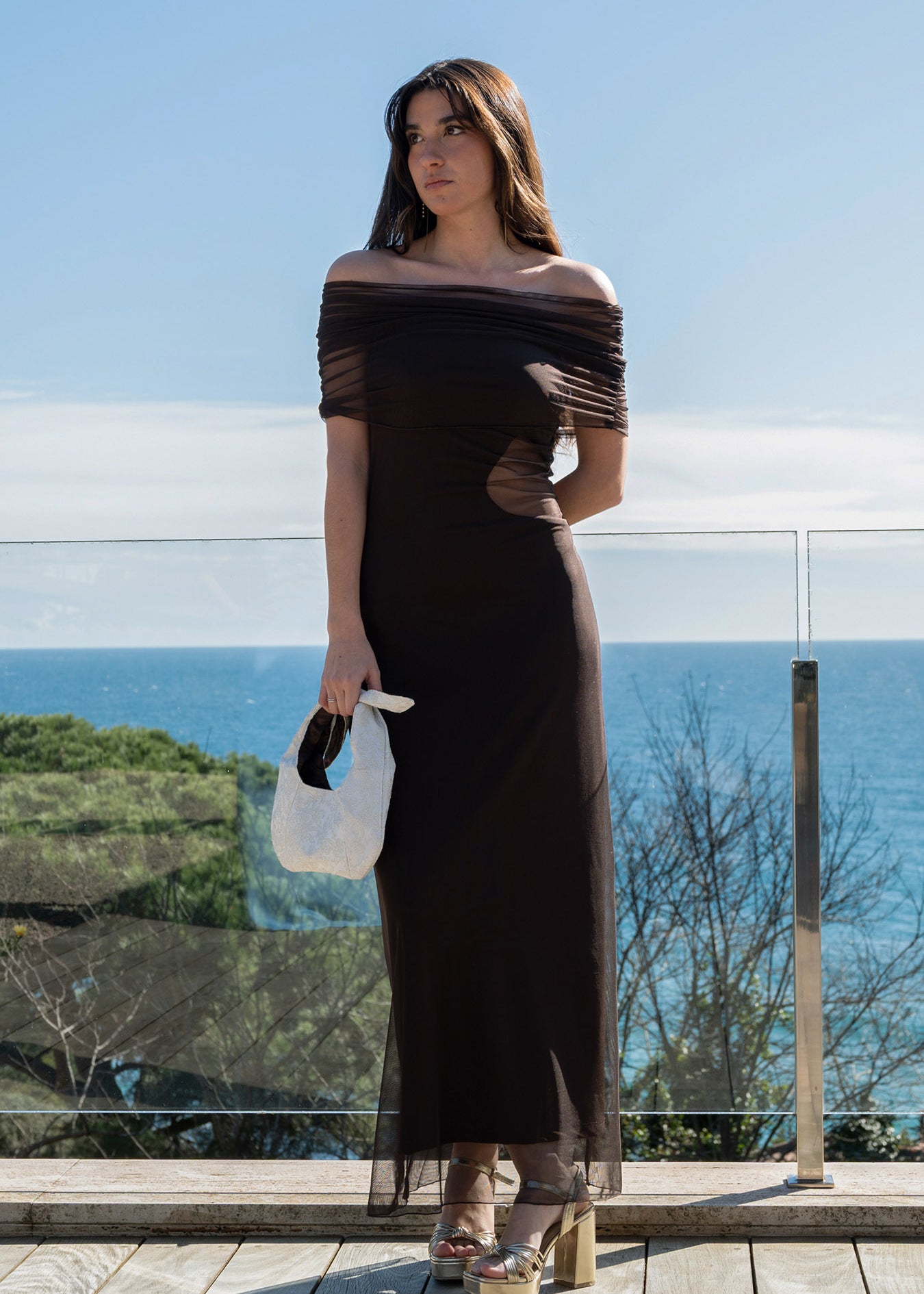 Isabella con el vestido First Step chocolate, luciendo el chal de tul sobre los hombros y bolso de mano blanco.