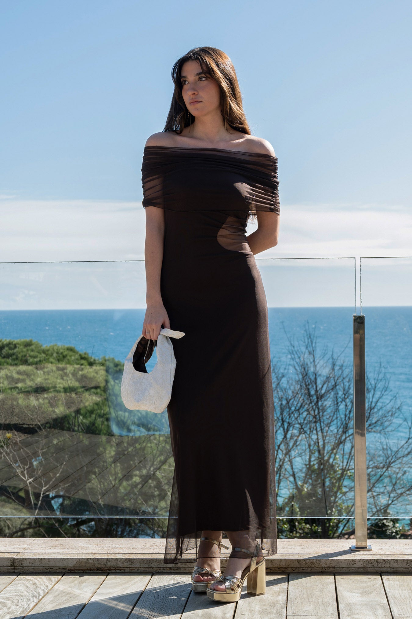 Isabella con el vestido First Step chocolate, luciendo el chal de tul sobre los hombros y bolso de mano blanco.