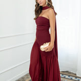 Modelo con vestido largo burdeos,  ideal para invitadas a bodas, fiestas de noche o eventos de gala. Escote palabra de honor que realza los hombros y el cuello, acompañado de un elegante fular integrado, aportando un toque sofisticado y original.