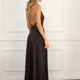 Modelo con vestido marrón chocolate, confeccionado en un tejido de licra con cuerpo que se adapta a la figura. Su escote halter y las delicadas piezas de tul en el cuello y la espalda abierta le dan un toque romántico y sutil.
La falda midi, con godetes que le aportan un movimiento fluido y ligero.