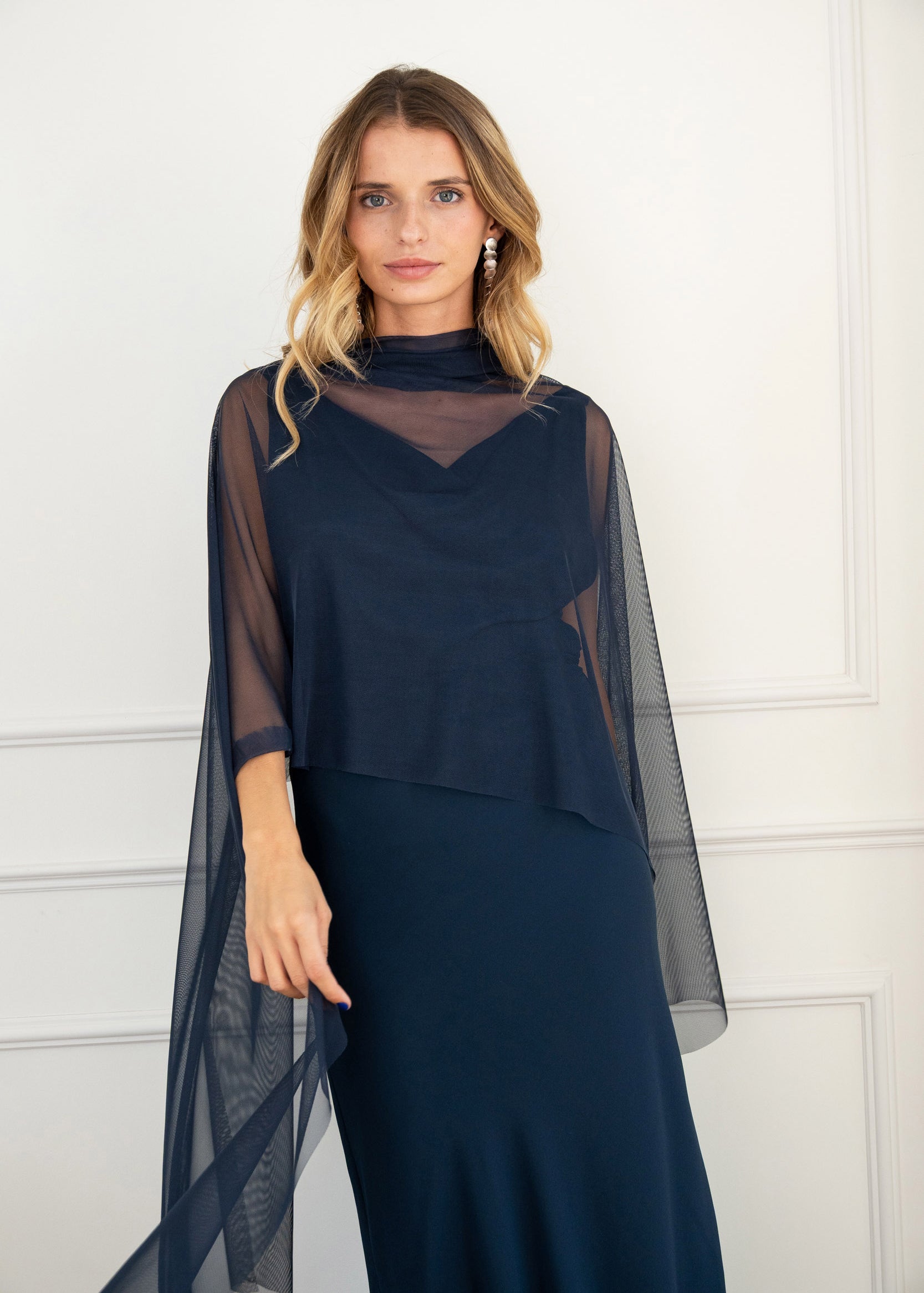 Modelo con vestido largo azul noche de silueta fluida con escote drapeado y espalda descubierta. Su tejido en gasa realza la figura con elegancia. Ideal para invitadas y eventos de otoño.