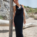 Vestido largo negro de lurex con escote drapeado y collar plateado en la playa