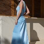Plano lateral de vestido largo de invitada multiposición color celeste con caída fluida y detalle de capa asimétrica.