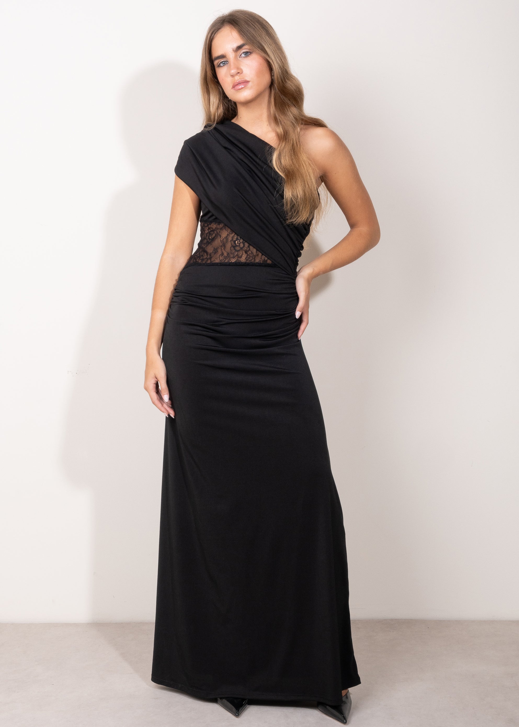 Modelo con vestido largo negro asimétrico, con detalle de encaje semitransparente en el torso y falda recta