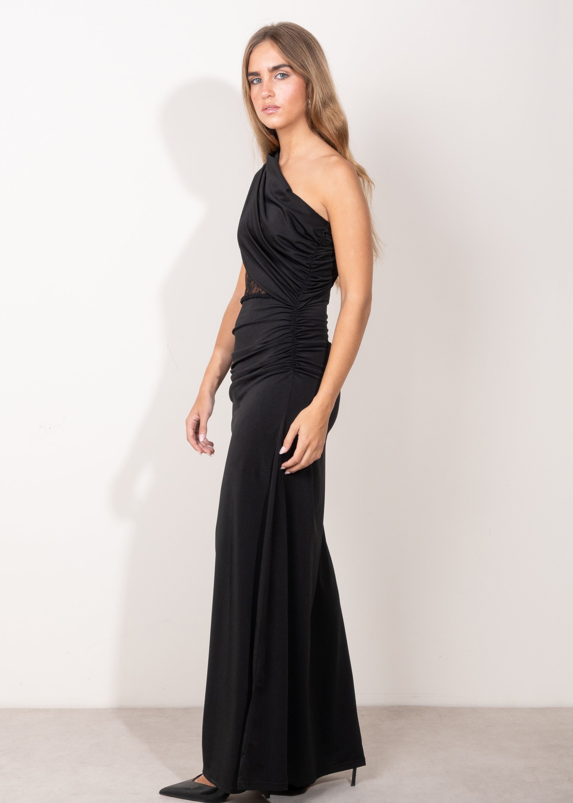 Modelo con vestido largo negro asimétrico, con detalle de encaje semitransparente en el torso y falda recta