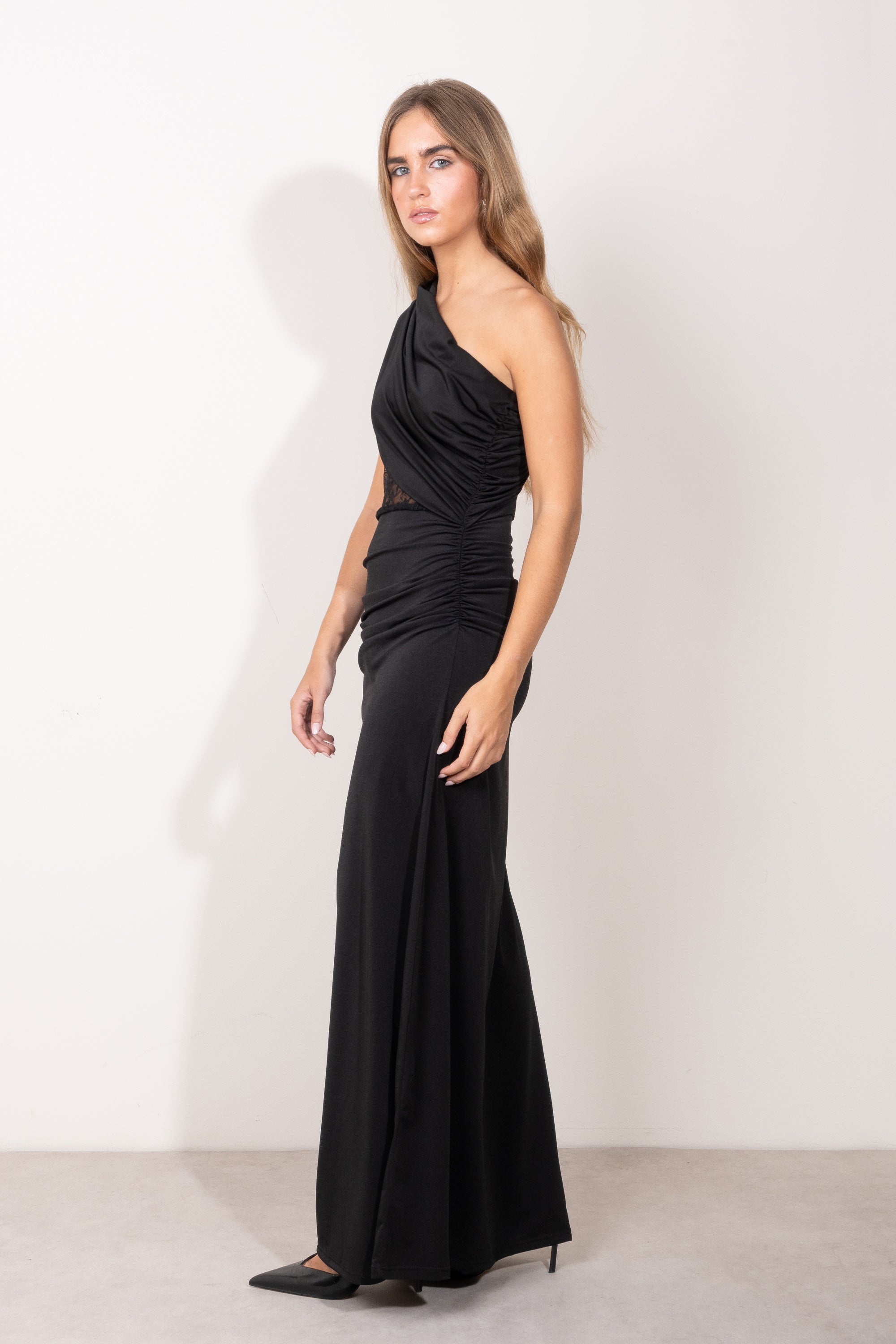 Modelo con vestido largo negro asimétrico, con detalle de encaje semitransparente en el torso y falda recta