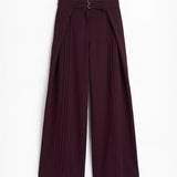 Pantalón berenjena de corte holgado con pliegues y doble hebilla para mujer, mostrado de frente sobre fondo blanco neutro.