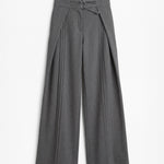 Pantalón gris de corte holgado con pliegues delanteros y doble hebilla para mujer, mostrado de frente sobre fondo blanco neutro.