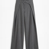 Pantalón gris de corte holgado con pliegues delanteros y doble hebilla para mujer, mostrado de frente sobre fondo blanco neutro.